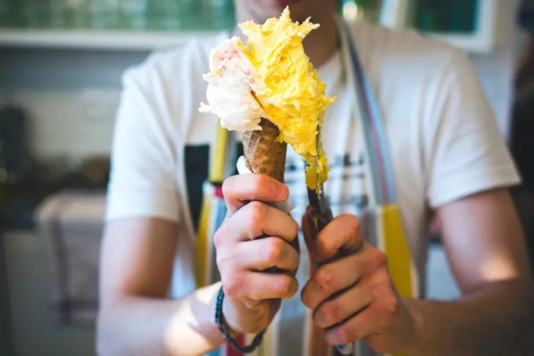 A vendor in an apron holding a cone of mango gelato